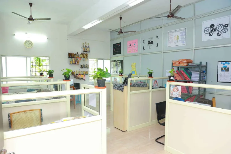 A staff room with partitioned desks, potted plants on the partitions and trophies on a shelf.