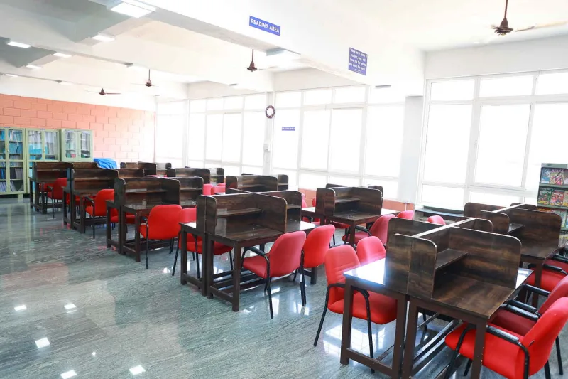 The library reading area: rows of wooden study carrels with red chairs, under tall windows.